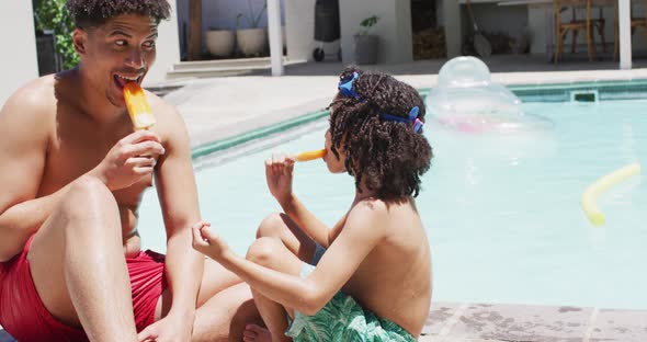 Happy biracial man and his son eating ice cream by swimming pool in garden