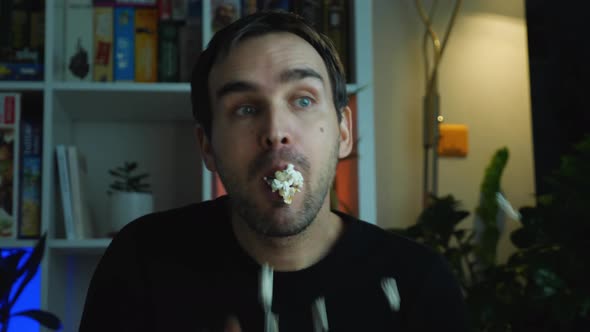 Close-up of a blue-eyed man watching TV in a dark room. A Caucasian man in black clothes is shovelin