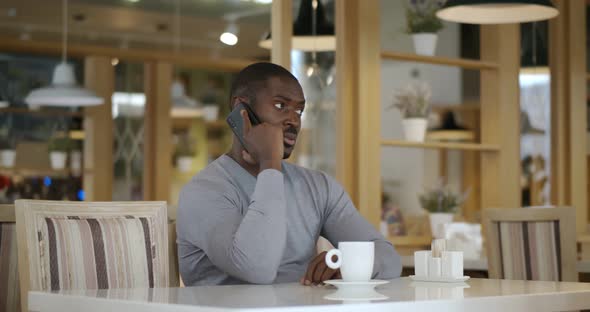 Happy African Man Speaking on Cellphone in Cafe