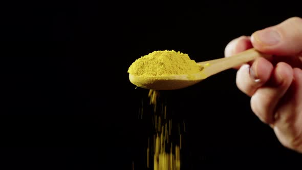 Adding Turmeric Powder to Dish on Black Background Using Seasoning and Flavors