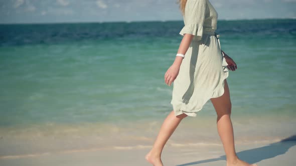 Woman In Hat Walks Along Beach On Caribbean Coast. Woman Relaxing On Seychelles Flowing Dress.