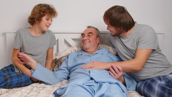 Aged Male Patient Embracing Kids and Talking While Lying on Bed at Home