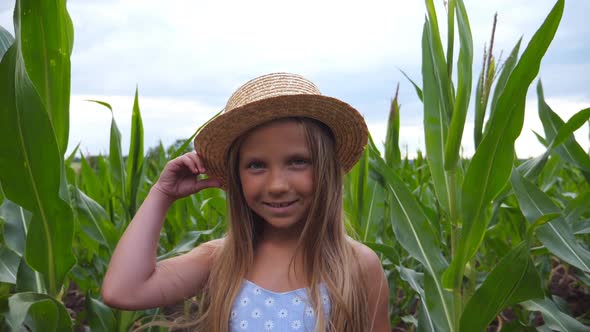 Portrait of Attractive Small Girl Looking Into Camera and Straightening Her Straw Hat Against