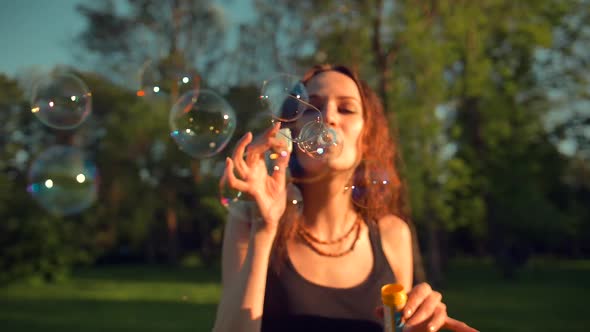 Front View of Young Pretty Adult Girl Making Soap Bubbles. Beautiful Tree with Orange Leaves.