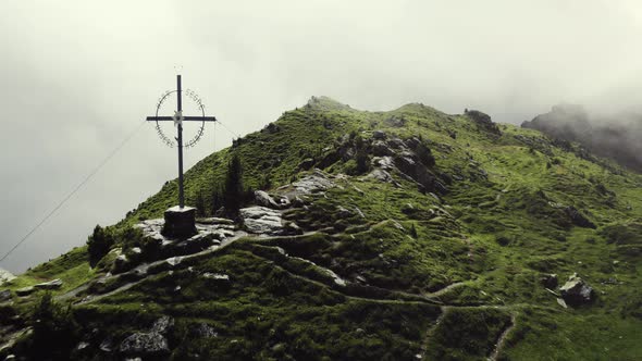 Aerial drone shot of a grass covered mountain top with a giant cross and a small trail leading along