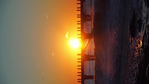 hot storm waves hit the pier at sunset. Beautiful orange sky, crashing waves.