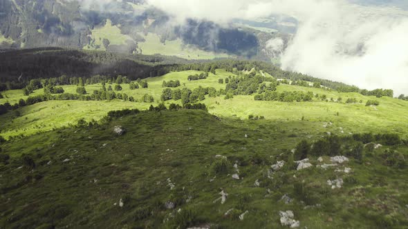 Aerial drone shot of a grass covered mountain top with a small trail leading up with clouds around.