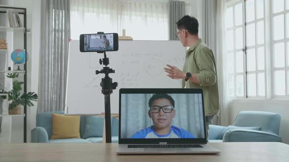 Asian Male Teacher Having Video Call On Laptop While Teaching Math Online With Boy Student At Home