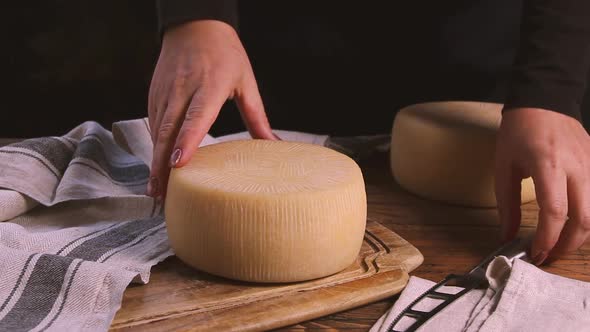 Women cut a wheel of  fresh homemade cheese on a wooden board with a cheese knife close up