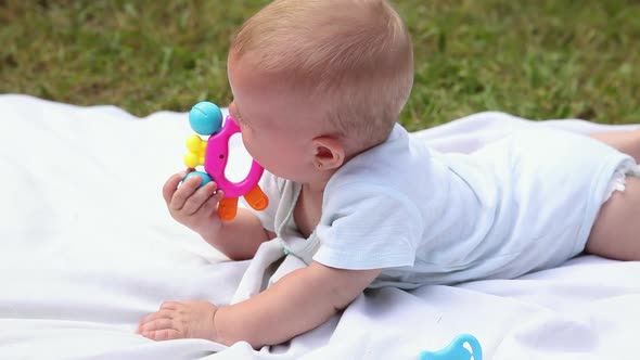 Little Newborn Girl Lying on Tummy Chewing Rattle on Blanket Summer Day Outdoor