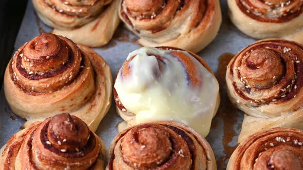 Pouring frosting on Freshly baked cinnamon rolls or Cinnabon close up. Sweet cream cheese frosting