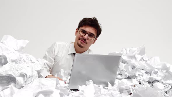 Office Man with laptop is waist-deep in crumpled papers dealing with bureaucracy