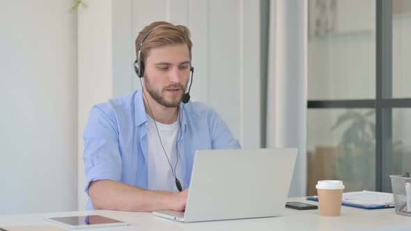 Creative Man Talking on Headset Working on Laptop in Office