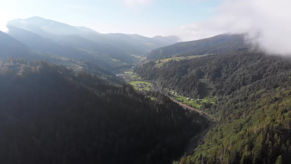 Flying Through the Clouds Over Carpathian Mountain Valley with Village in Summer