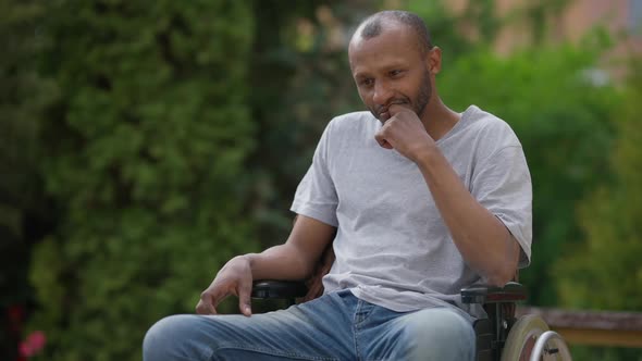 Medium Shot Portrait of Thoughtful African American Man Sitting in Wheelchair Outdoors