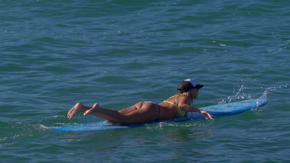 A young woman in a bikini paddling on a longboard surfboard.