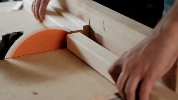 Close up of carpenter worker using saw cutting wooden plank on construction site.