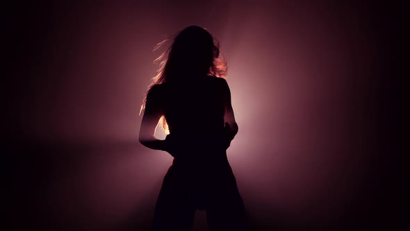 Silhouette of Beautiful Dancer on Smoky Dark background.Spotlight Shines Back