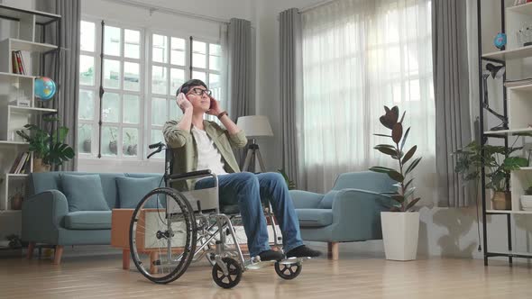 Asian Man Sitting In A Wheelchair Listening To Music With Headphones In Living Room