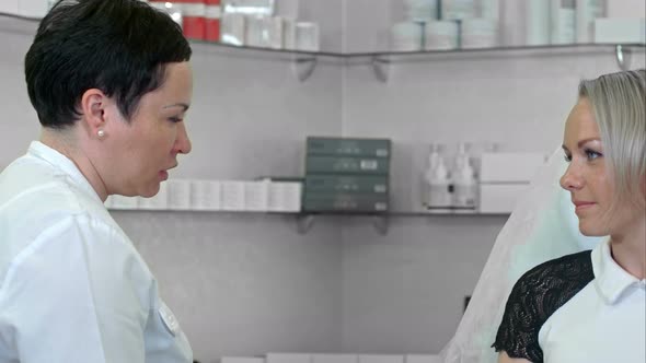 Cosmetologist Talking with Female Client in Bathrobe Sitting in the Cosmetologist Office