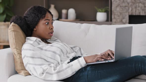 African Girl Student Freelancer User Lies on Sofa at Home Looking at Laptop Using Internet Checks