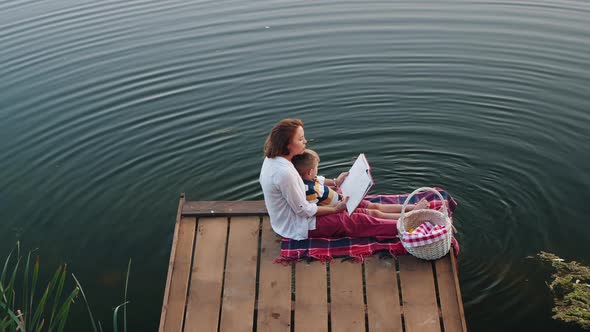 Top View of a Mom Reads a Book To Little Son on the Lake