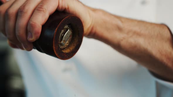 Close up: the chef is using pepper mill to add some pepper to food, pepper is falling