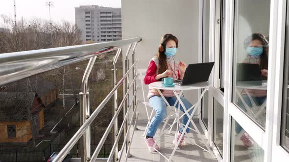 Teenager Girl in Mask and Headphones, Listening To Music on Laptop, Chatting Online, on Open Balcony