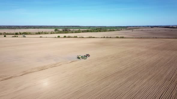 Aerial view of tractor with harrow system plowing ground on cultivated farm field