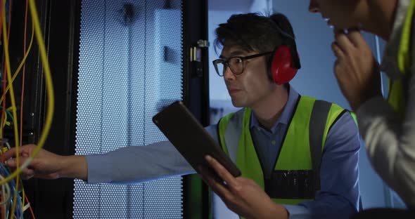 Diverse female and male it technicians wearing headphones using tablet checking computer server