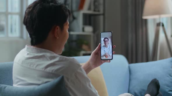 Man Having Video Call With A Doctor On Smartphone While Lying On Sofa In The Living Room