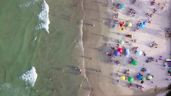 Aerial top down shot of small waves breaking on Bombas beach full of tourists at golden hour. Dolly