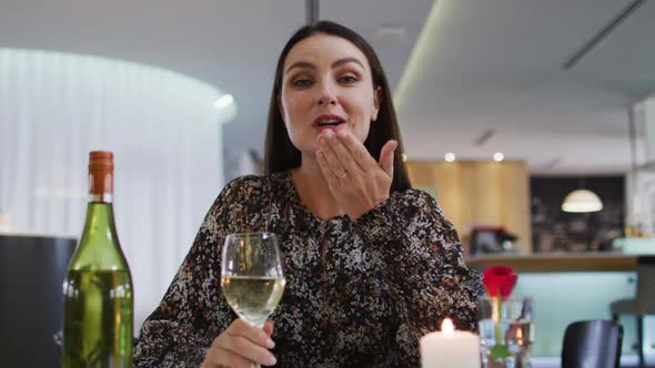 Caucasian woman having romantic dinner at restaurant holding wine glass and blowing kiss to camera