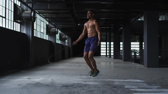 Shirtless african american man skipping the rope in an empty urban building