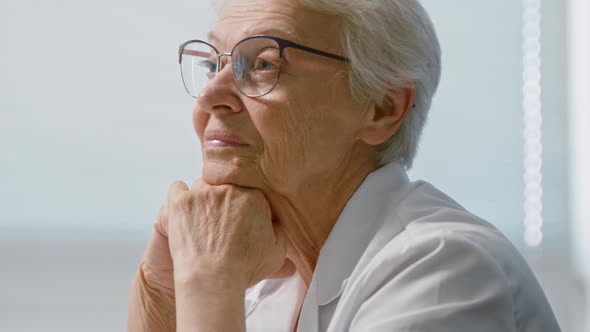 Smiling senior woman doctor with elegant glasses leans on wrinkled hands