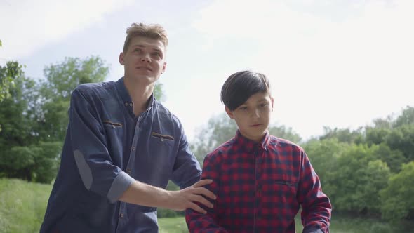 Adorable Young Father Teaching His Son To Ride the Scooter in the Park. The Guy Supports the Kid