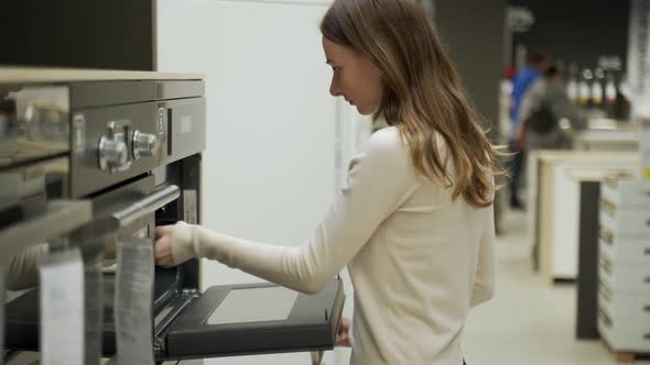 Woman Chooses an Oven in a Supermarket Store