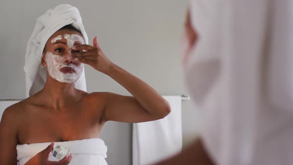 African american woman applying face mask looking in the mirror at bathroom