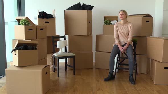 A Happy Moving Woman Sits on a Chair and Looks Thoughtfully Around an Empty Apartment