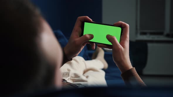 Man Lying on Couch Using Smart Phone with Chroma Key Green Screen at Night, Scrolling Through Social