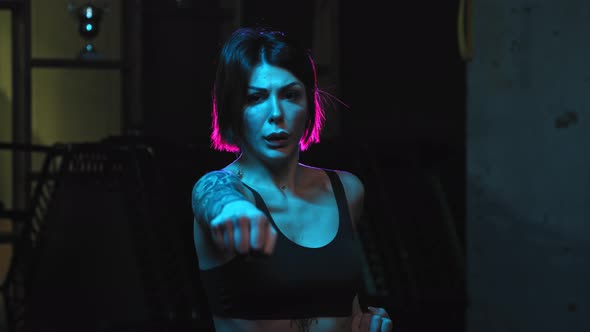 A Strong Tattooed Woman Showing Karate Fighting Moves in Neon Lighting