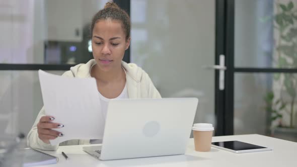 African Woman with Laptop Having Loss While Reading Documents