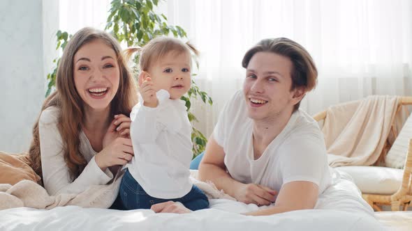 Caucasian Young Parents Happy Mother and Caring Father Lie on Bed with Little Girl Child Toddler