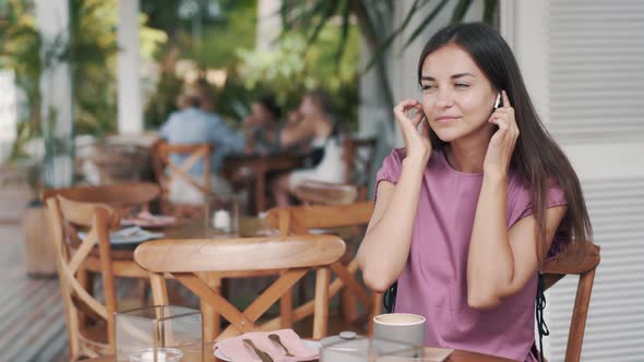 Young Woman Puts on Wireless Earphones, Listens To Music and Dances in Cafe