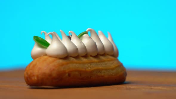 Sweet Eclair Rotating on a Wooden Table on a Blue Background