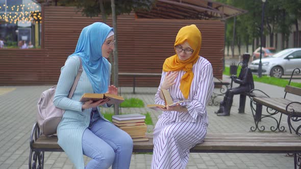 Two Muslim Women Students in Traditional Scarves with Textbooks in Their Hands Communicate in the