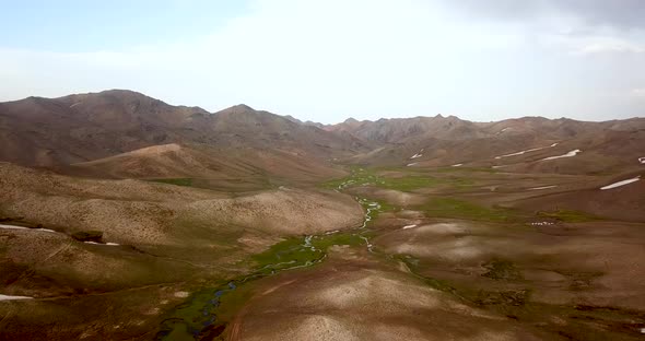 Fresh brown hills and green meadow with small rivers in highlands with mountain landscape in backgro