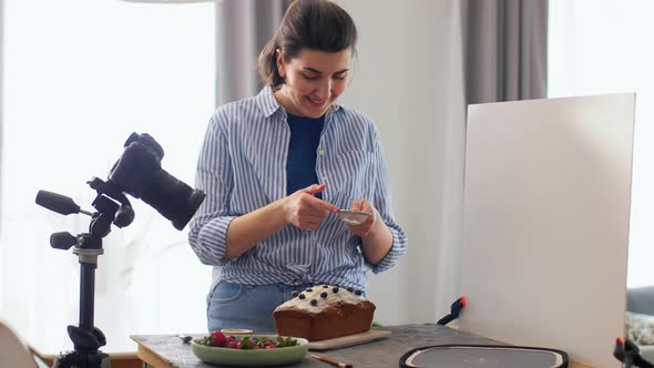 Food Blogger with Camera Icing Cake in Kitchen