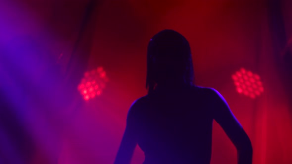 Silhouette of Dancing Joan of Arc on Stage in a Dark Studio with Smoke and Neon Lighting. A Bright