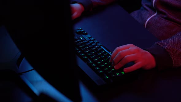 A Young Man Is Playing Computer. Hands Working on the Keyboard Close-up. Blue and Red Light Falls on